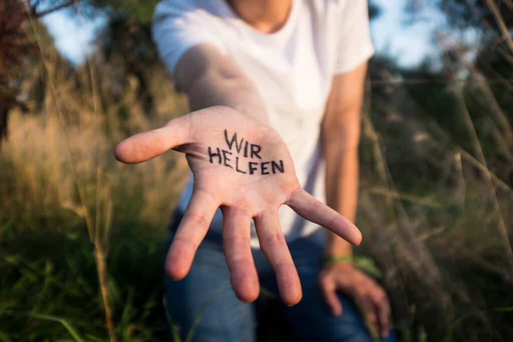 Eine Person streckt eine Hand zu uns. "Wir helfen" steht auf der Handinnenfläche